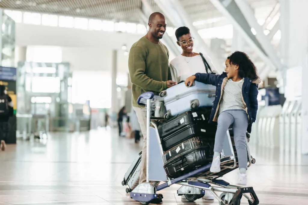 young-daughter-sitting-on-luggage-trolley-with-her-parents-at-international-airport-african-family-waiting-at-airport-for-their-flight-JLPSF05972